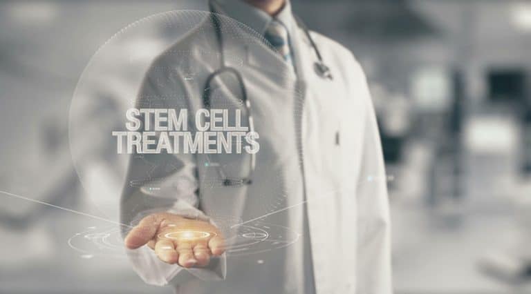 A doctor in a white coat with a stethoscope holds out his hand, displaying a digital hologram with the words STEM CELL TREATMENTS—highlighting elite healthcare and the promise of future medical advances in a modern medical setting.