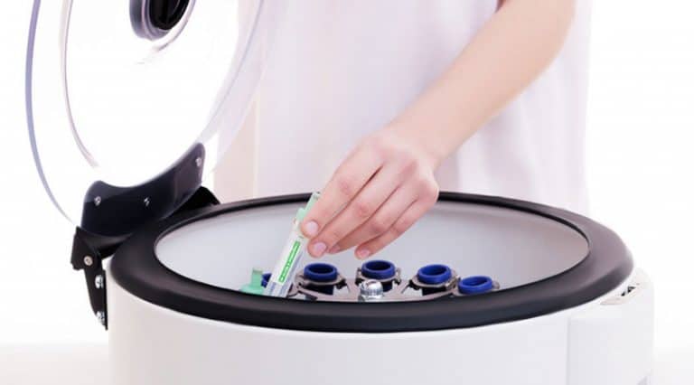 A person places a test tube into a centrifuge machine with an open lid, preparing to spin and separate stem cells. The new technology features multiple slots for efficient sample processing.