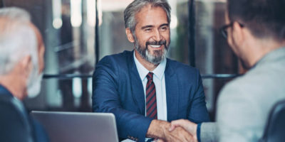 Confident business man shaking hands with two guys smiling.