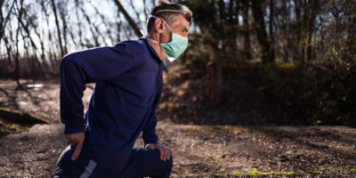 Man stretching with mask on while running.