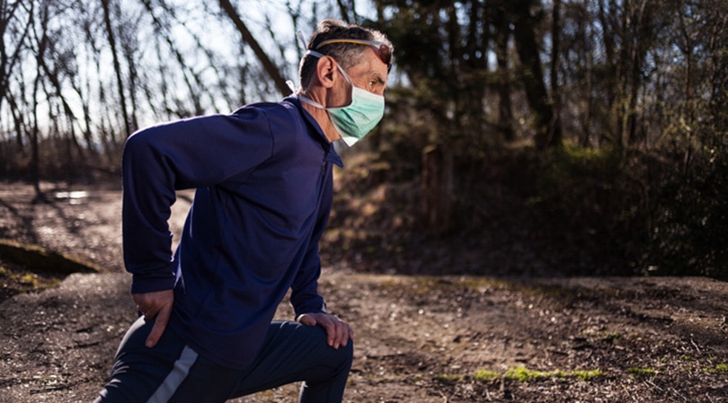Man stretching with mask on while running.