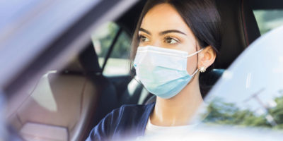 Closeup of woman driving car while wearing face mask.