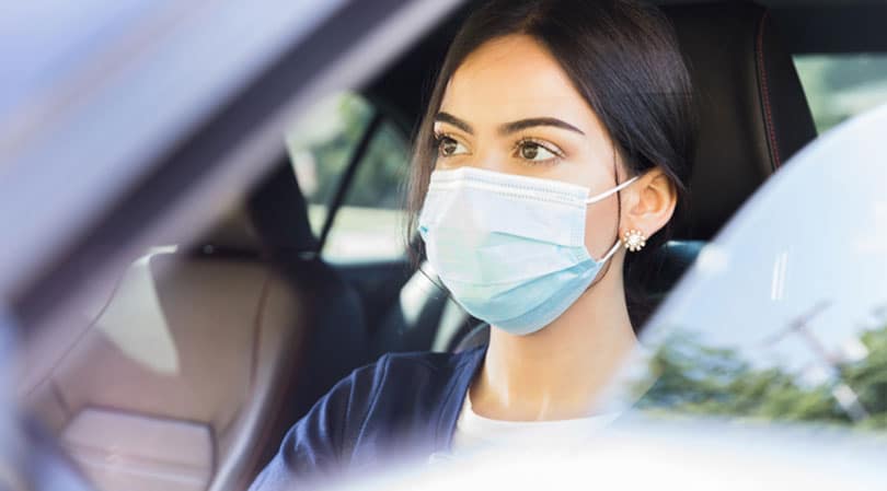 Closeup of woman driving car while wearing face mask.