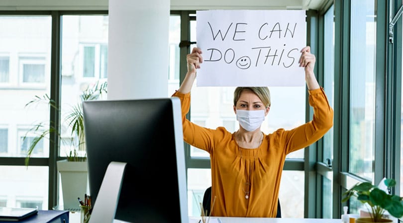 Woman holding up a sign while wearing a face mask in an office.