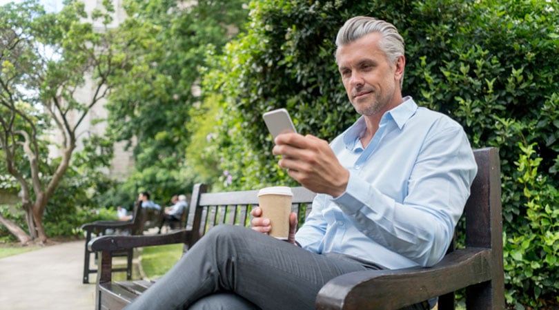 Business man sitting on bench looking at phone.