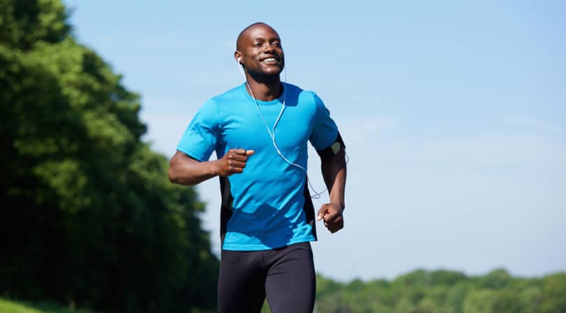 Black man running with green trees and a blue shirt.