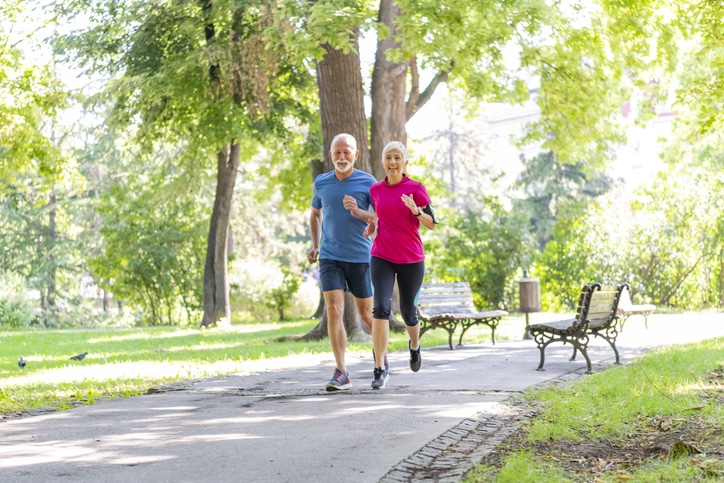 Mature Sporty Couple Jogging Outdoors in Nature. Two Elderly Athlete Persons is Running in the Park on a Sport Track During a Warm Sunny Day.