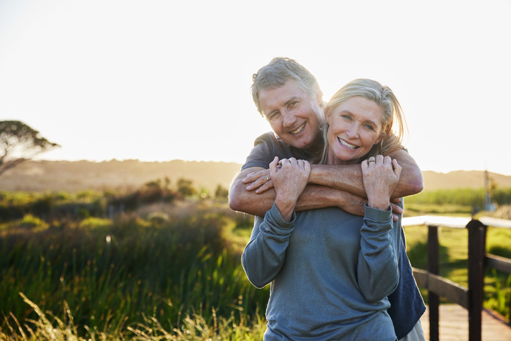 Portrait of an affectionate mature couple standing arm in arm and smiling during a walk together in a nature reserve in summer