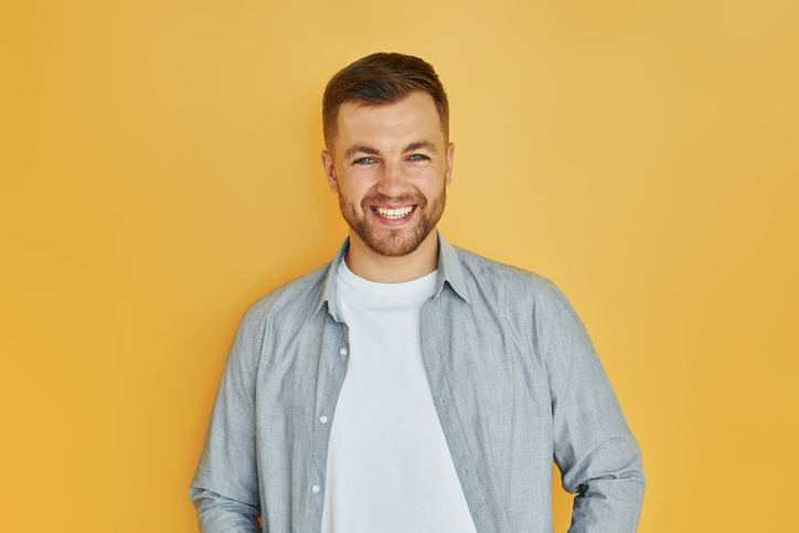 Young man in casual clothes standing indoors in the studio and demonstrates emotions.