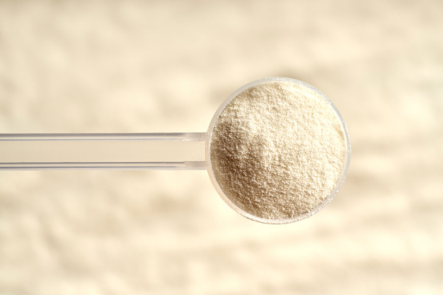 A clear plastic scoop filled with fine, off-white collagen powder, viewed from above against a blurred, light-colored background.