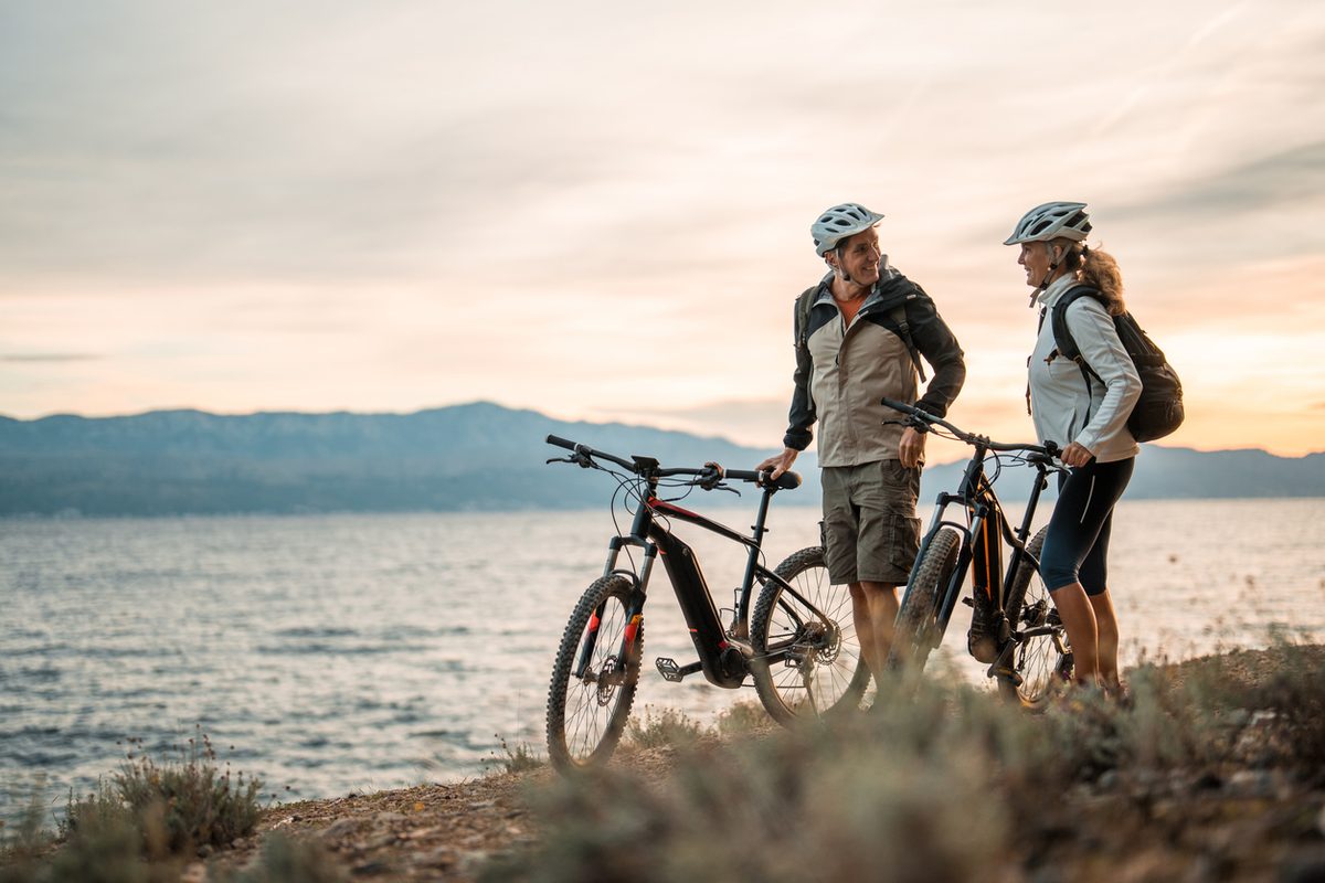 Couple riding bicycles beside a lake at sunset