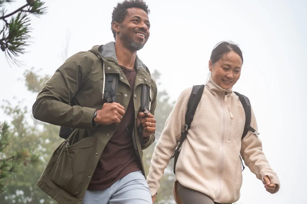 A man and a woman wearing backpacks hike together outdoors in the fog.