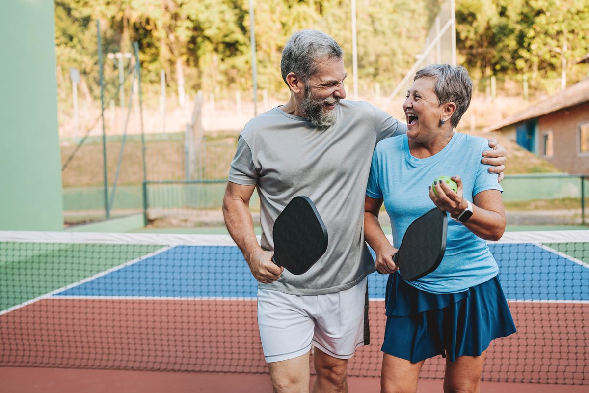 Older couple laughing as they walk off a pickleball court together