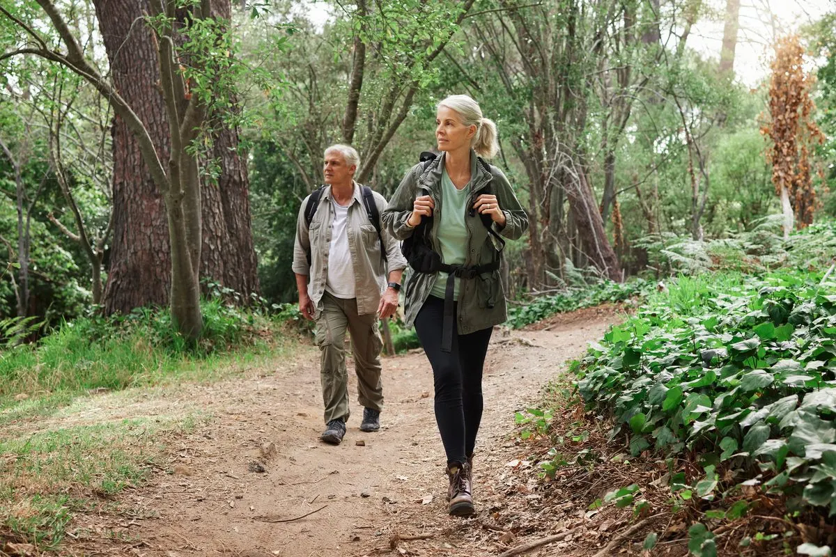 A middle-aged man and woman with backpacks hiking along a dirt forest trail.