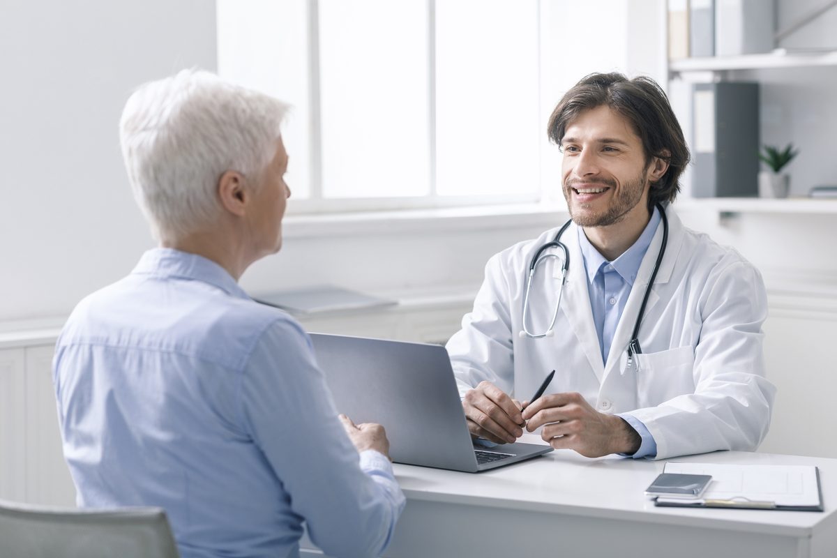 A doctor at a desk with a laptop talks with an older patient