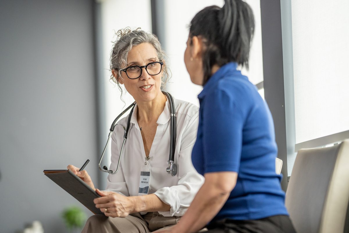 A physician takes notes while talking with a patient during a consultation