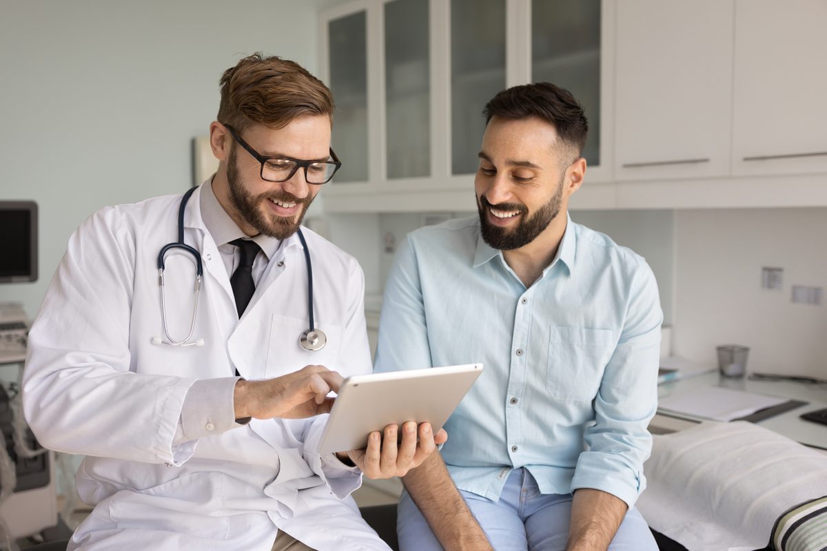 A physician reviews information on a tablet with a smiling male patient