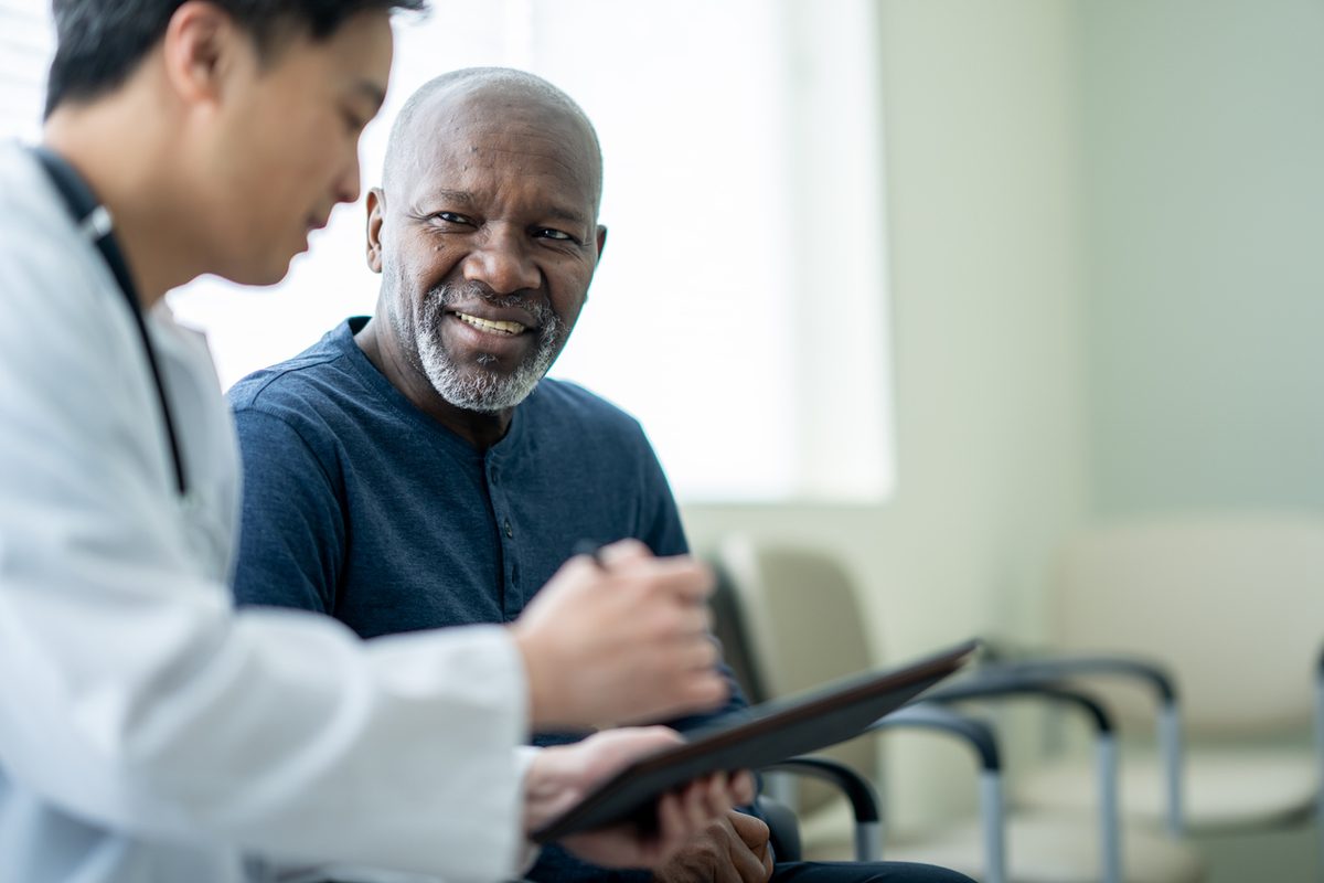 A doctor reviews a treatment plan on a tablet with a smiling older patient