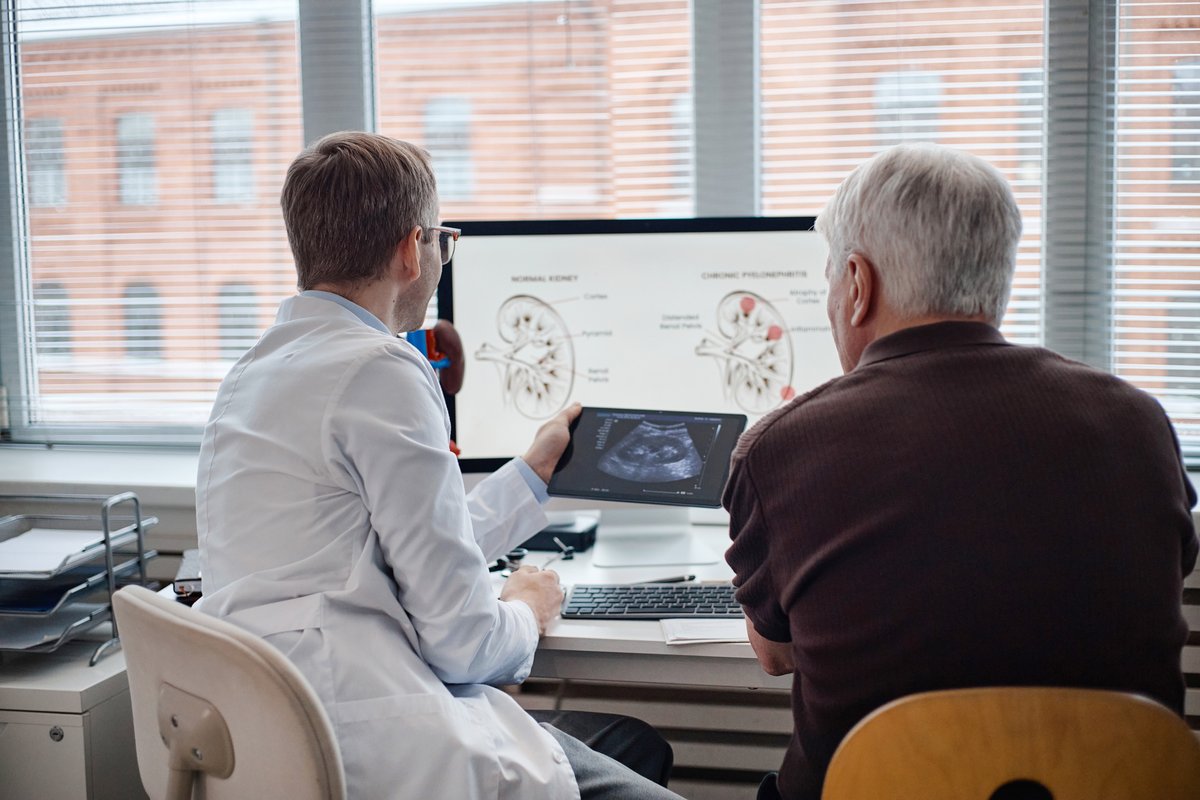 A doctor in a white coat showing a digital tablet with an ultrasound image to an older patient in an office.