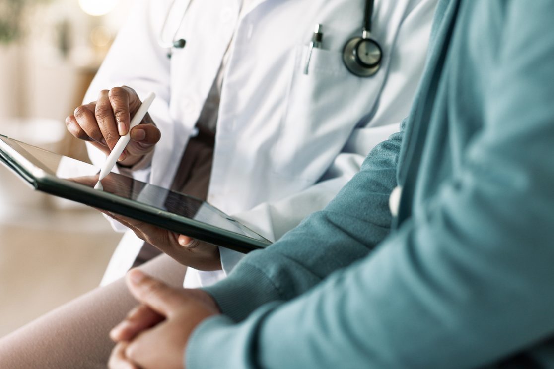 A physician takes notes on a tablet while talking with a patient