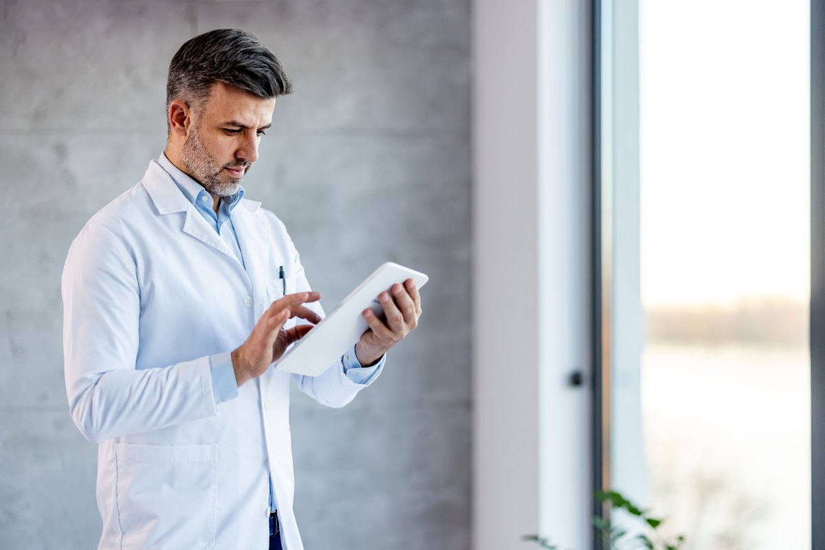 A male doctor in a white lab coat using a tablet.
