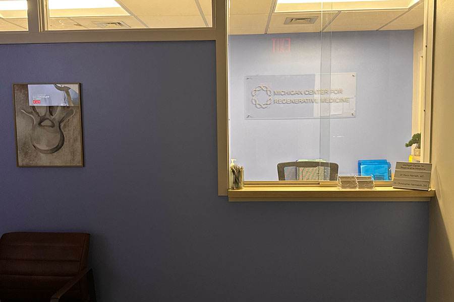 Interior view of the Michigan Center for Regenerative Medicine reception area in Grand Rapids, featuring an anatomical drawing of a spine on the wall and a desk sign listing the doctors in the office.
