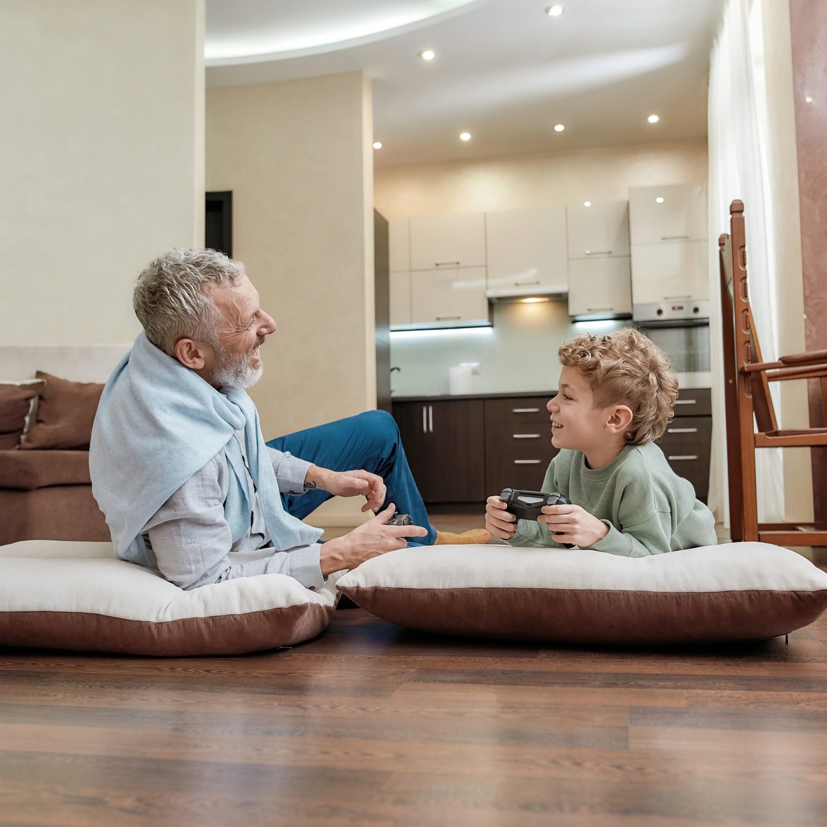 An older man and a young boy lying on floor cushions playing video games together.