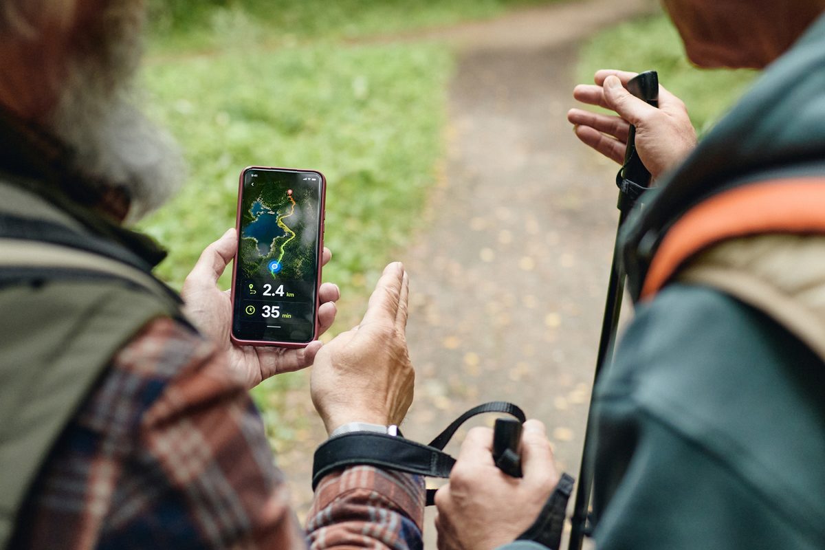 Two hikers holding trekking poles look at a smartphone displaying a trail navigation app.