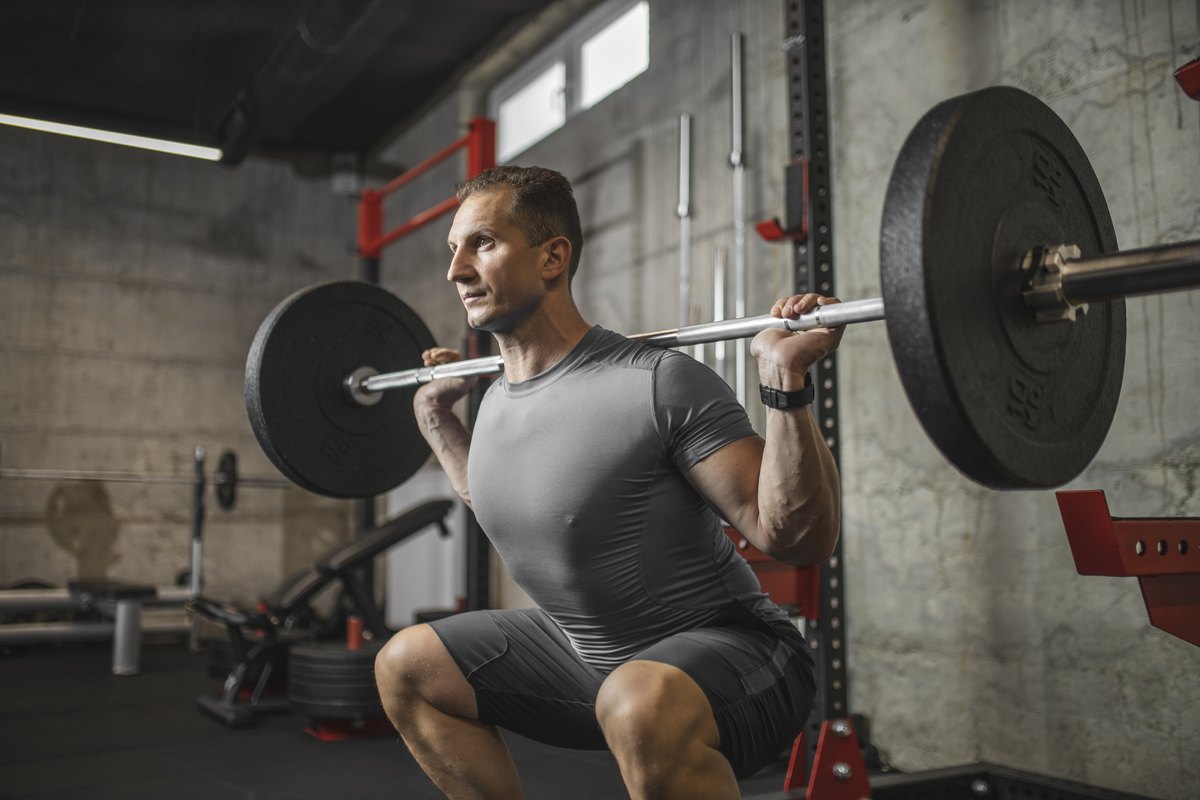 A man in athletic wear performing a barbell back squat in a gym