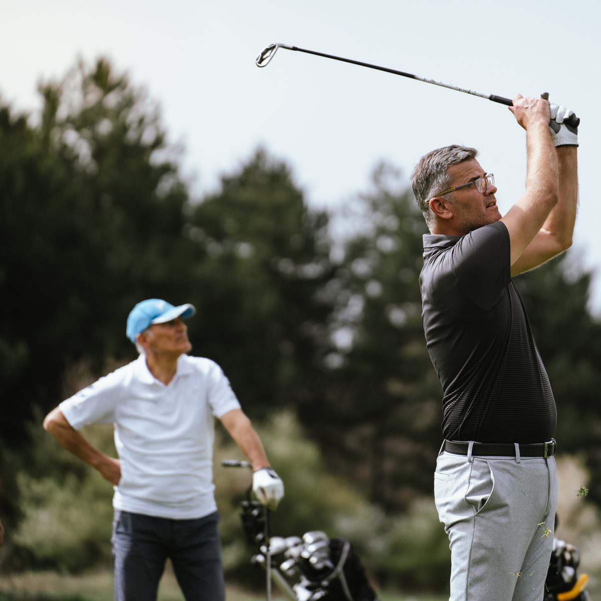 A man swings a golf club while another man watches from behind on a golf course.