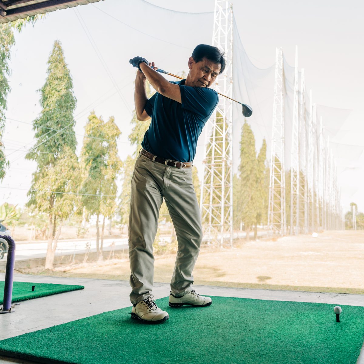 A man in a blue polo shirt swings a golf club at a driving range.