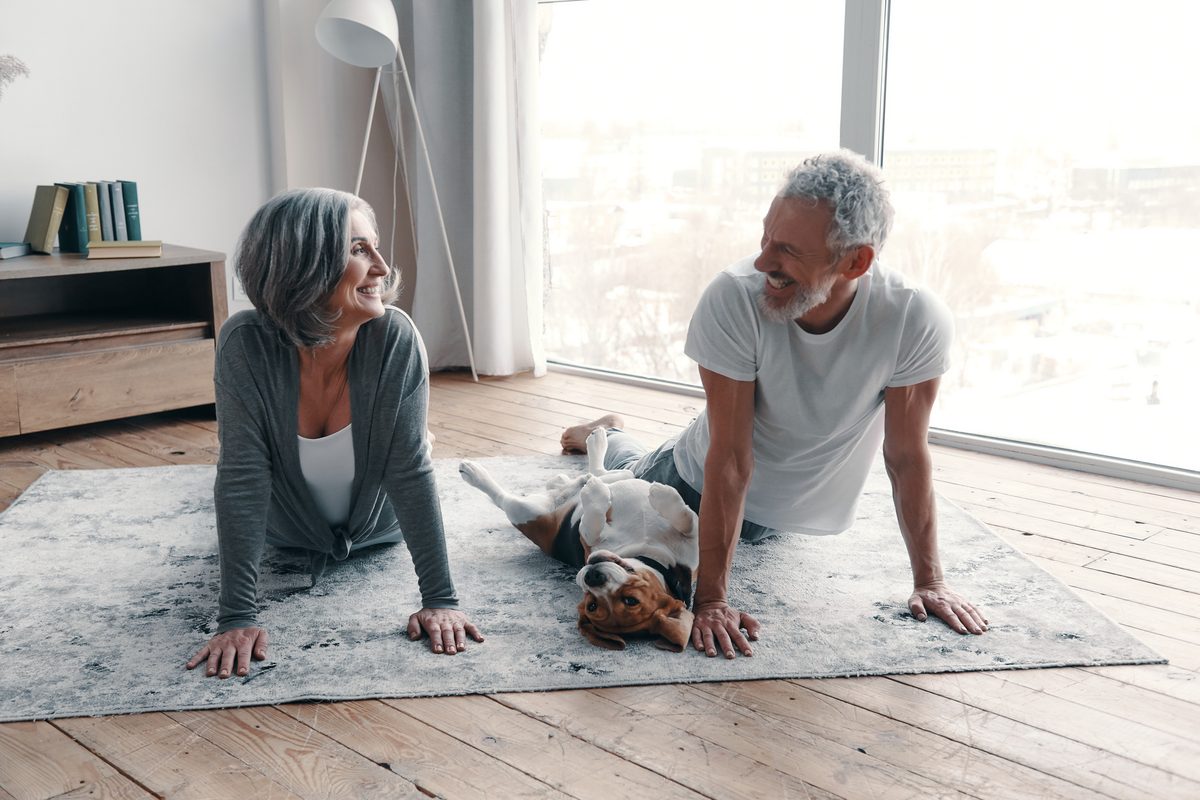 Older couple stretching together at home with their dog nearby