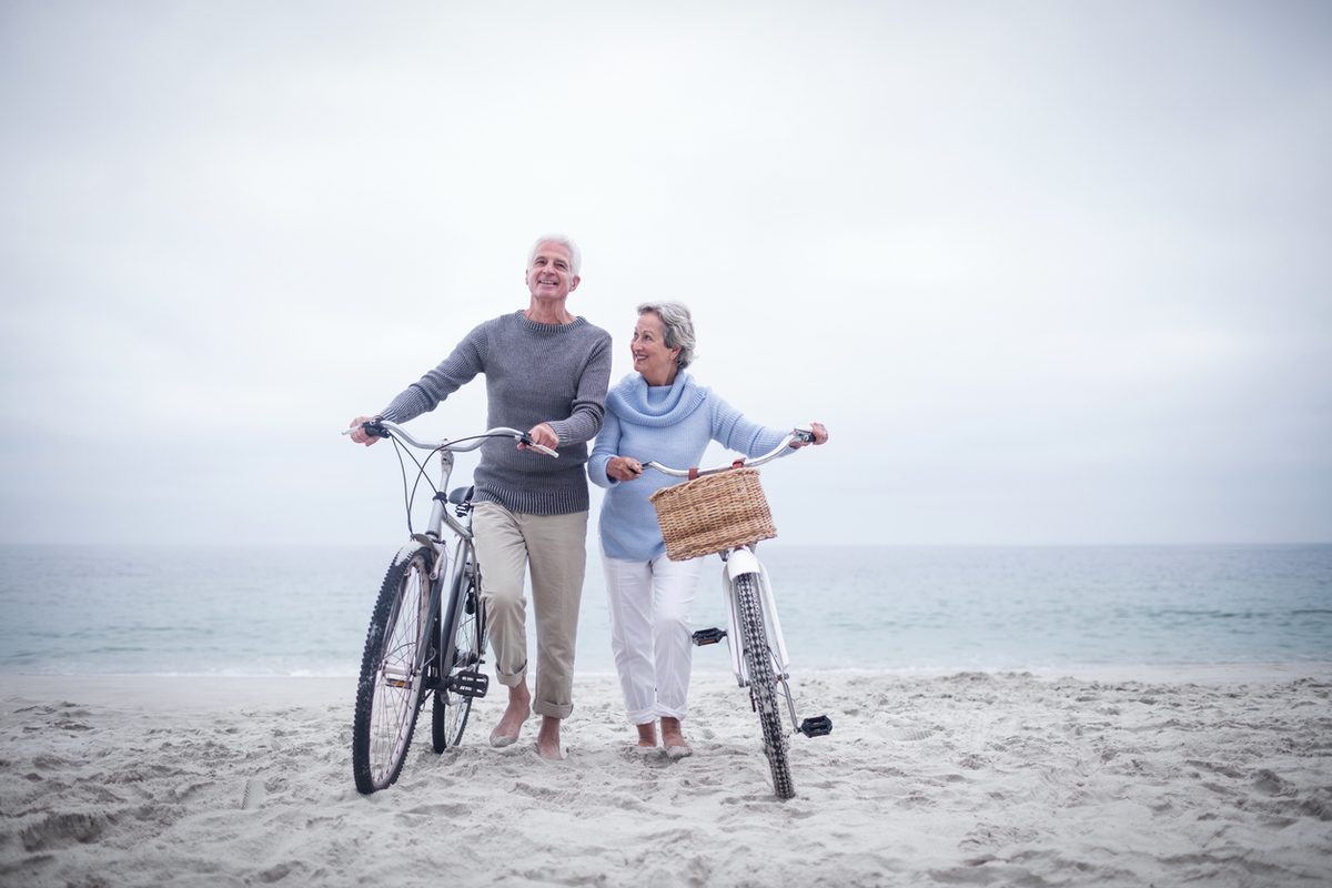 Older couple smiling as they walk their bikes along a sandy Lake Michigan beach