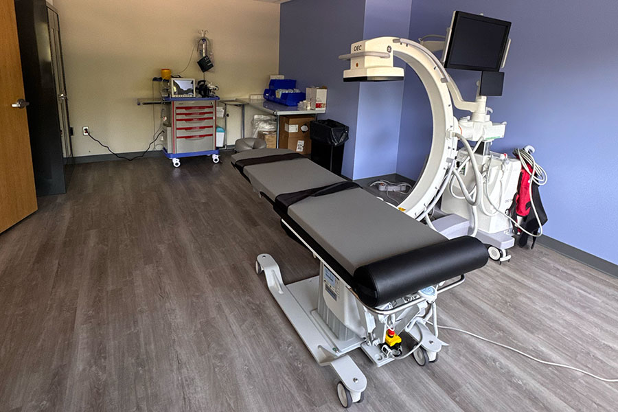 Medical procedure table with an OEC C-arm imaging system in a Grand Rapids office clinic room.