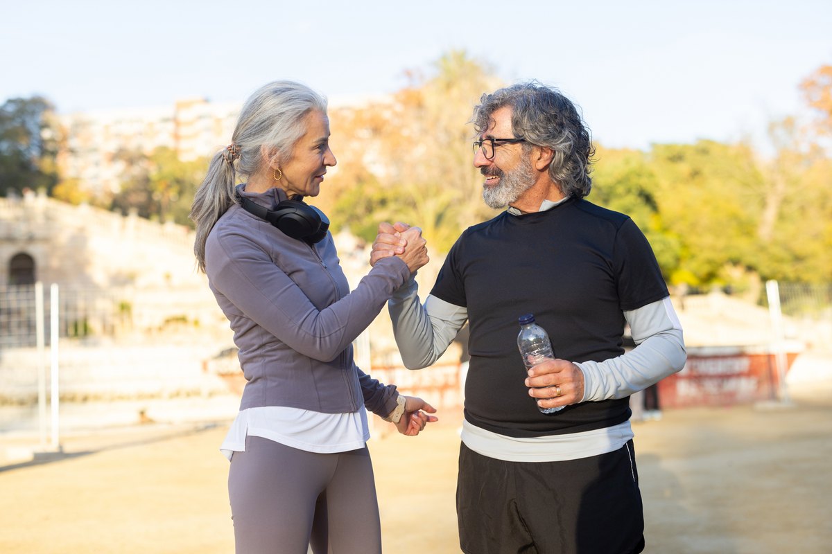 An older man and woman in athletic wear smiling and shaking hands while standing outdoors.