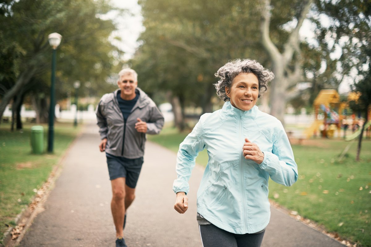 A middle-aged man and woman jogging along a park path.