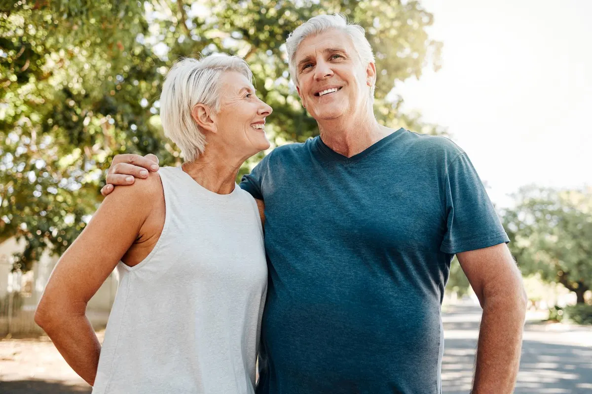 An older couple smiling and looking at each other outdoors with their arms around one another.