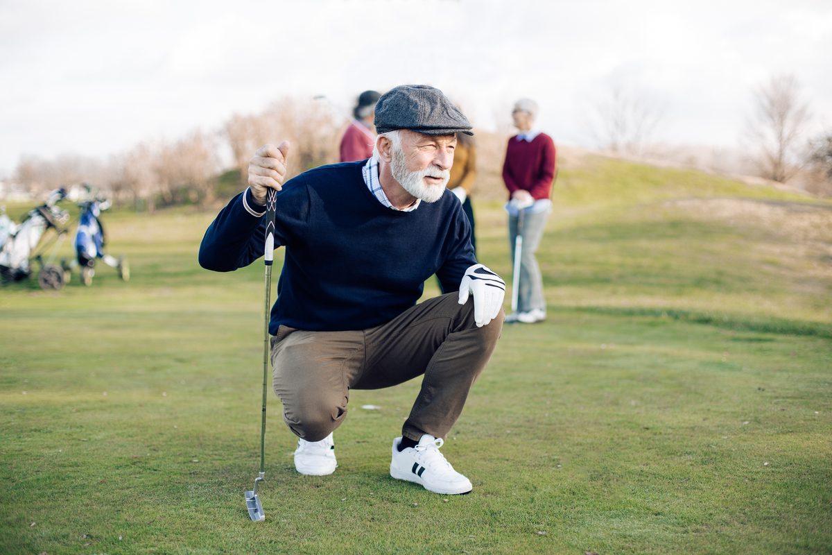 Senior golfer crouching to read the green