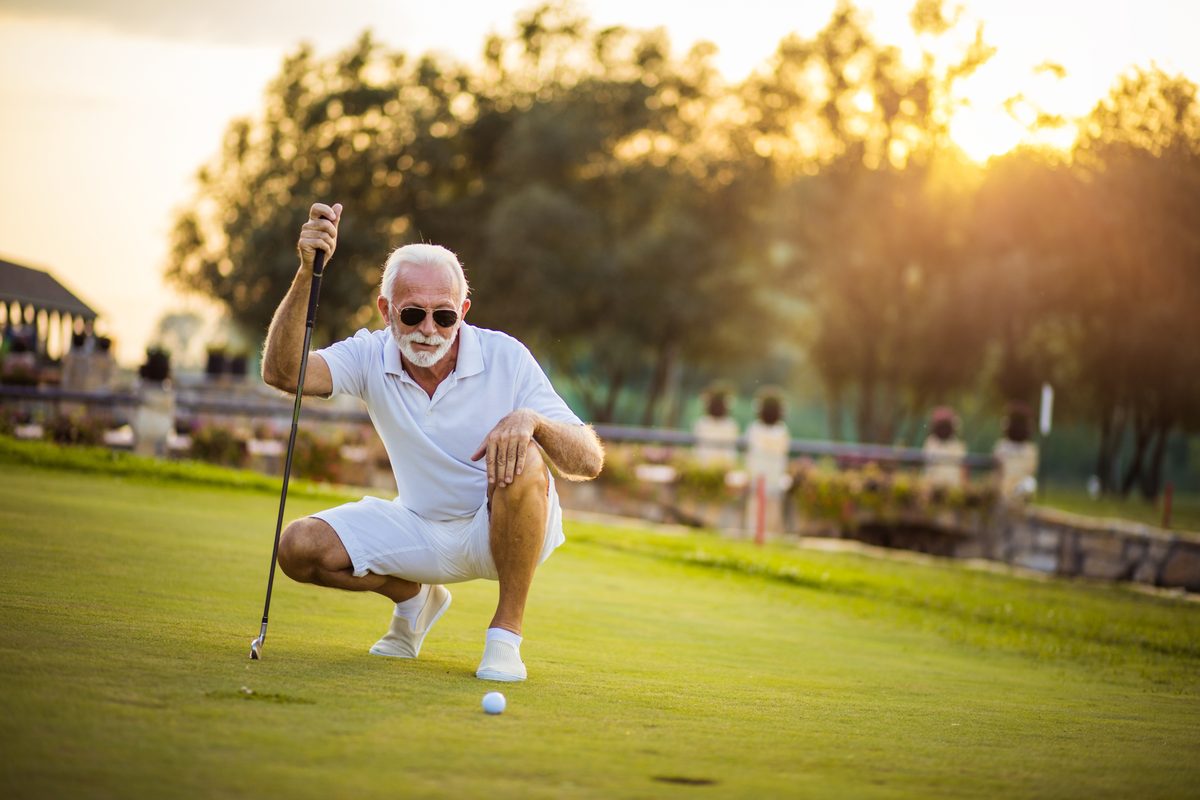Senior golfer reading a putt at sunset