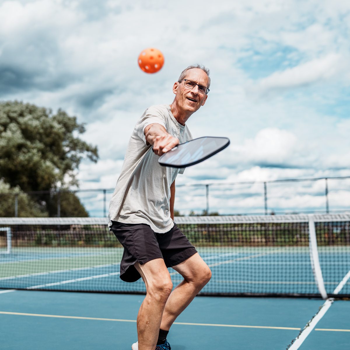 A man playing pickleball on an outdoor court, about to hit an orange ball with his paddle.