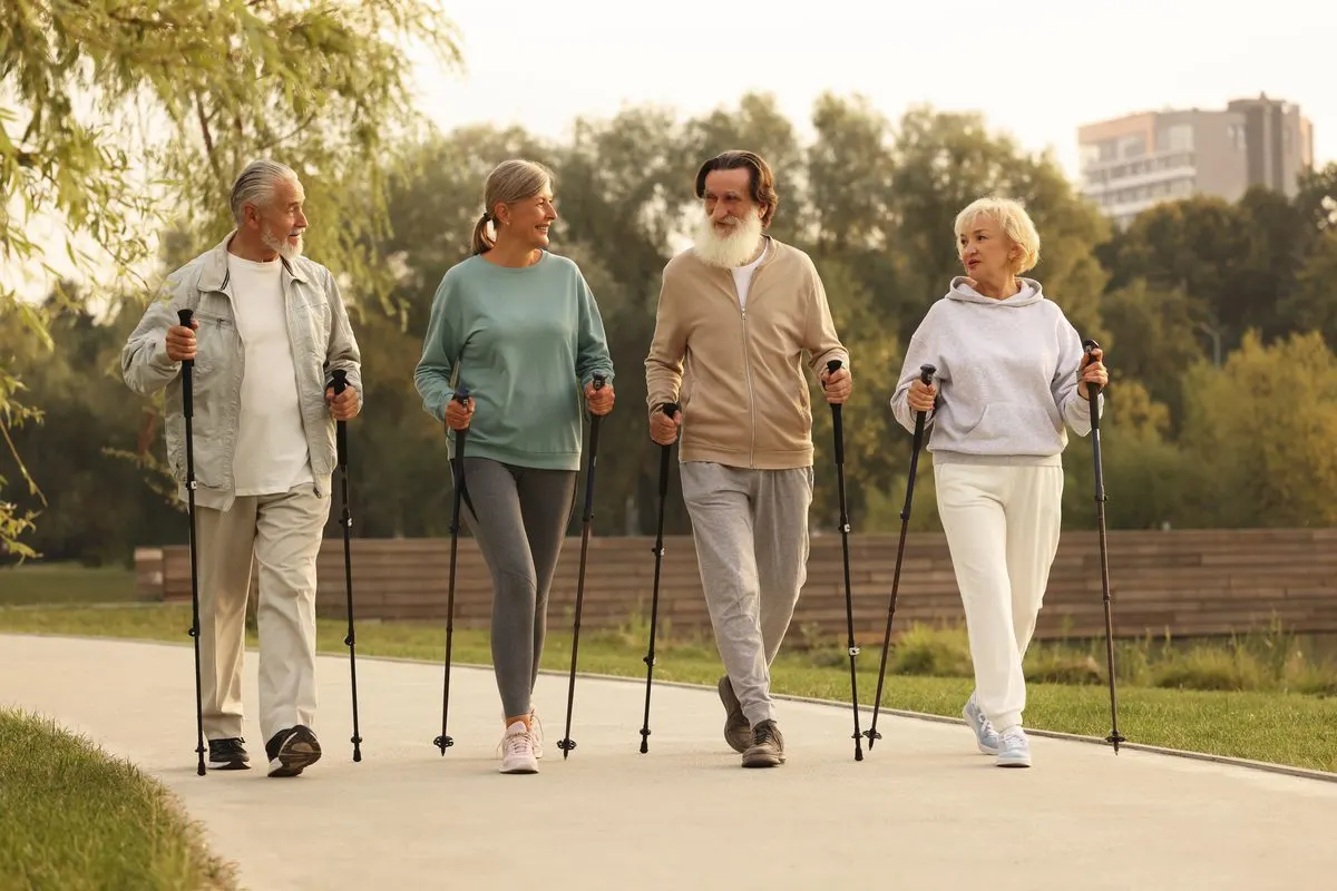 Four older adults walking along a paved park path using Nordic walking poles.