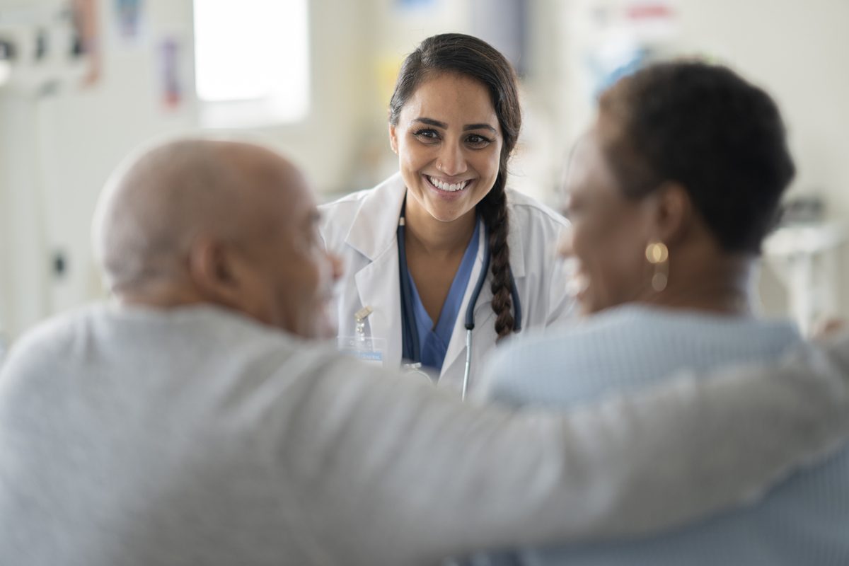A smiling doctor greets an older couple at the start of a consultation