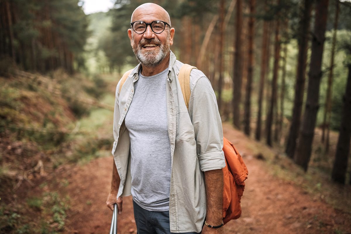 A smiling man hikes along a forest path