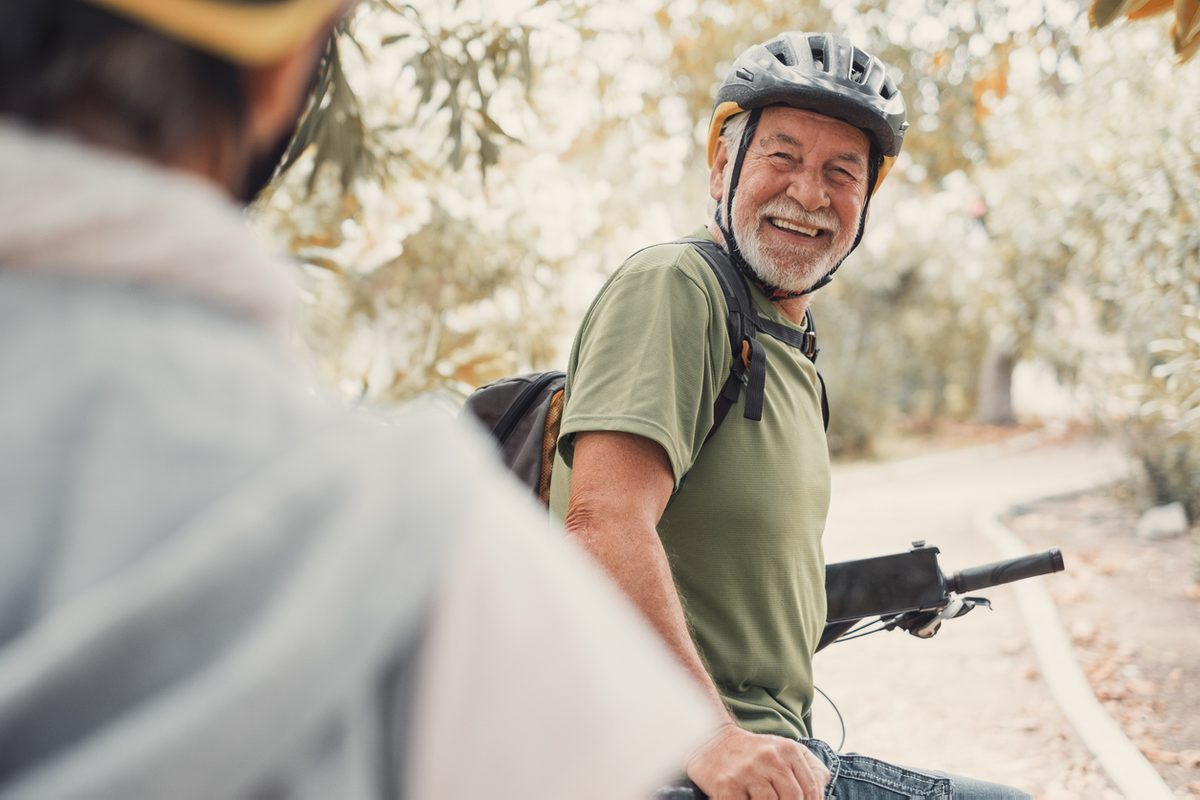 Smiling older man riding a bicycle on a wooded trail