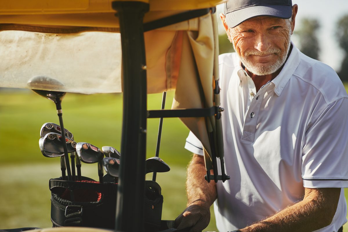 Smiling senior golfer at a golf cart