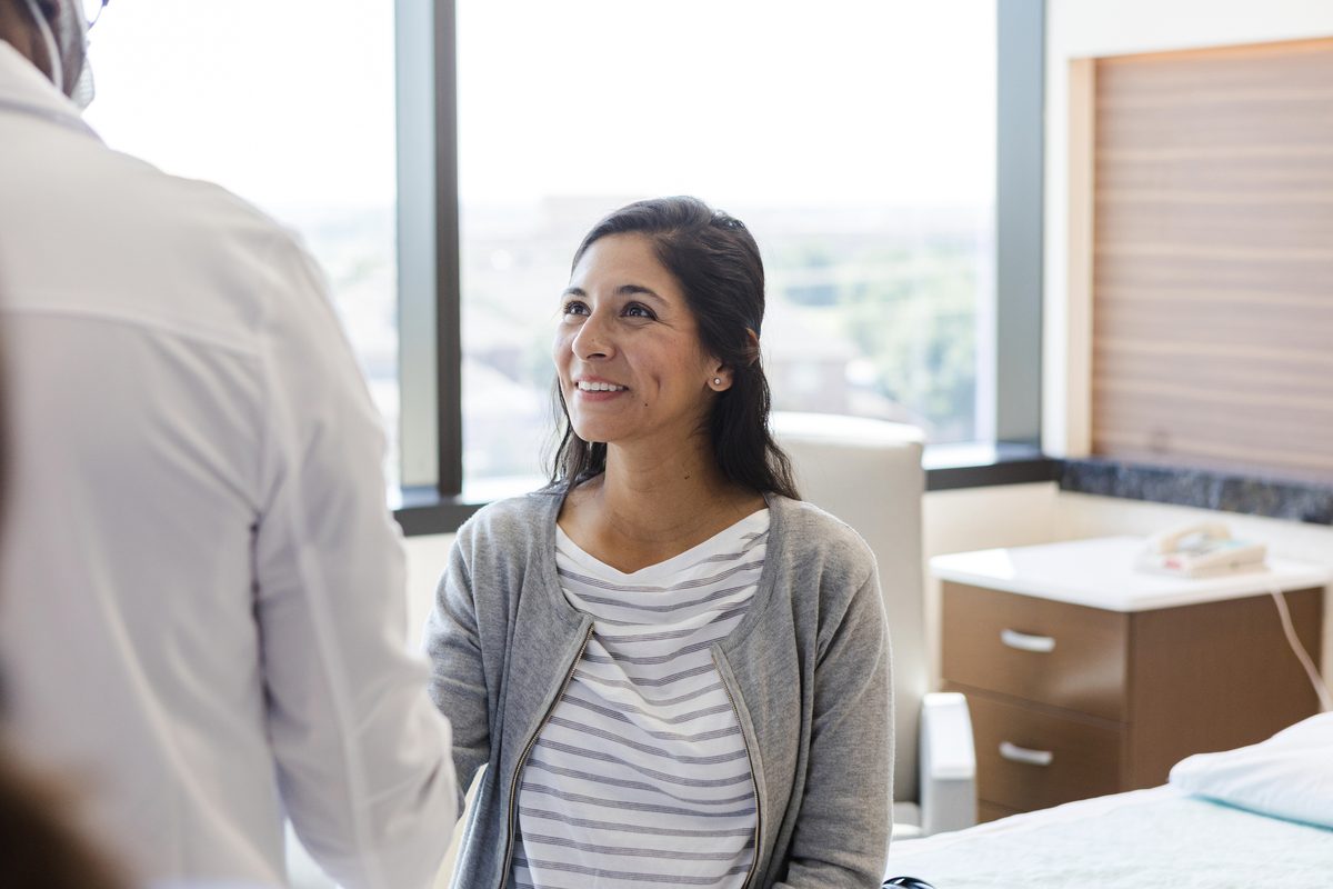 A smiling woman talks with a doctor in the exam room