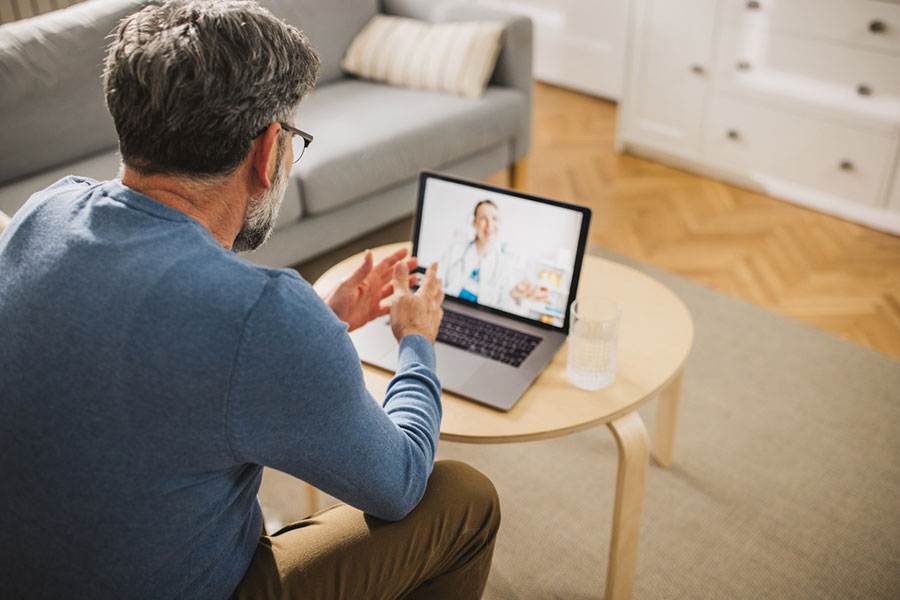 A man at home has a video consultation with a doctor from a Michigan pain clinic on his laptop to discuss chronic pain treatment.