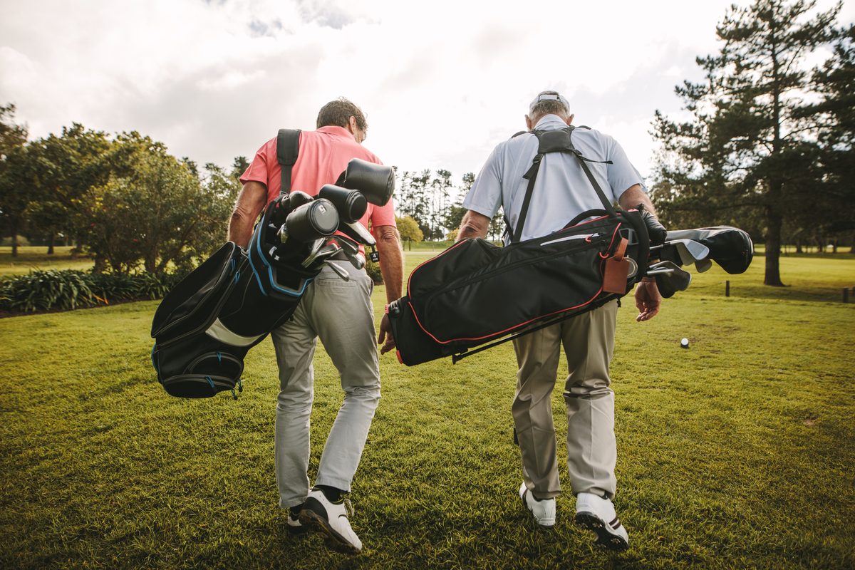 Two golfers carrying bags down the fairway