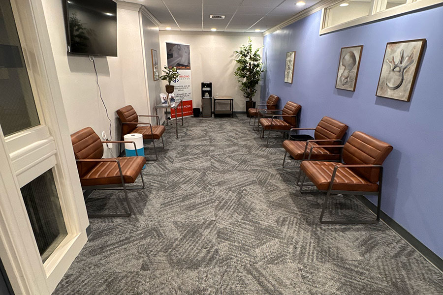 Waiting room in a Grand Rapids office with brown leather chairs arranged along white and blue walls, featuring patterned carpet, a water cooler, and medical diagrams on the wall.