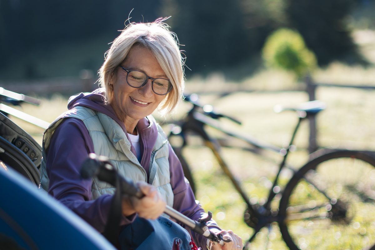 A woman wearing glasses and a vest preparing a bicycle near a car.